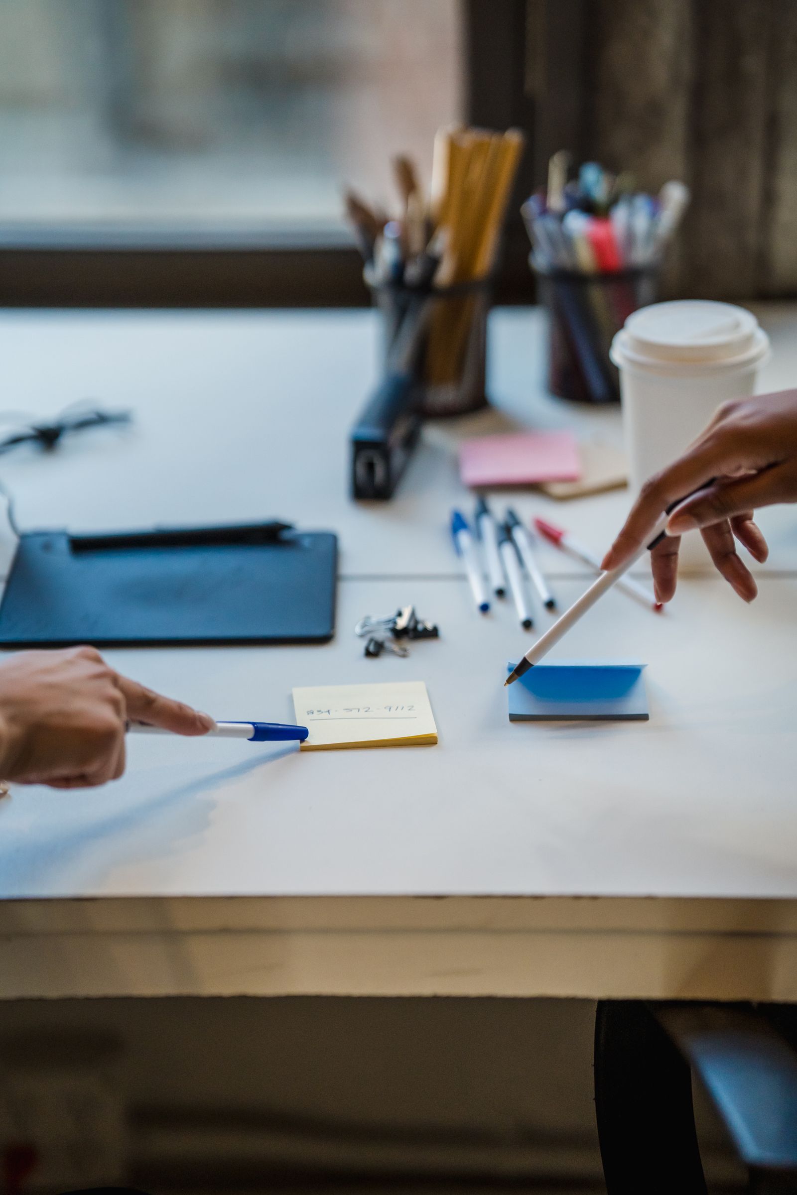 Close-up of two people planning work together with notes and pens